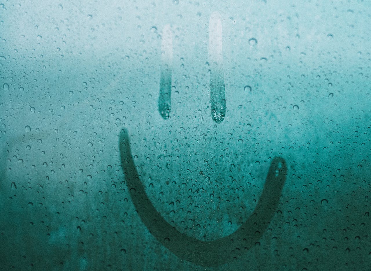 A smiley face drawn on a wet window, featuring water drops after the rain.